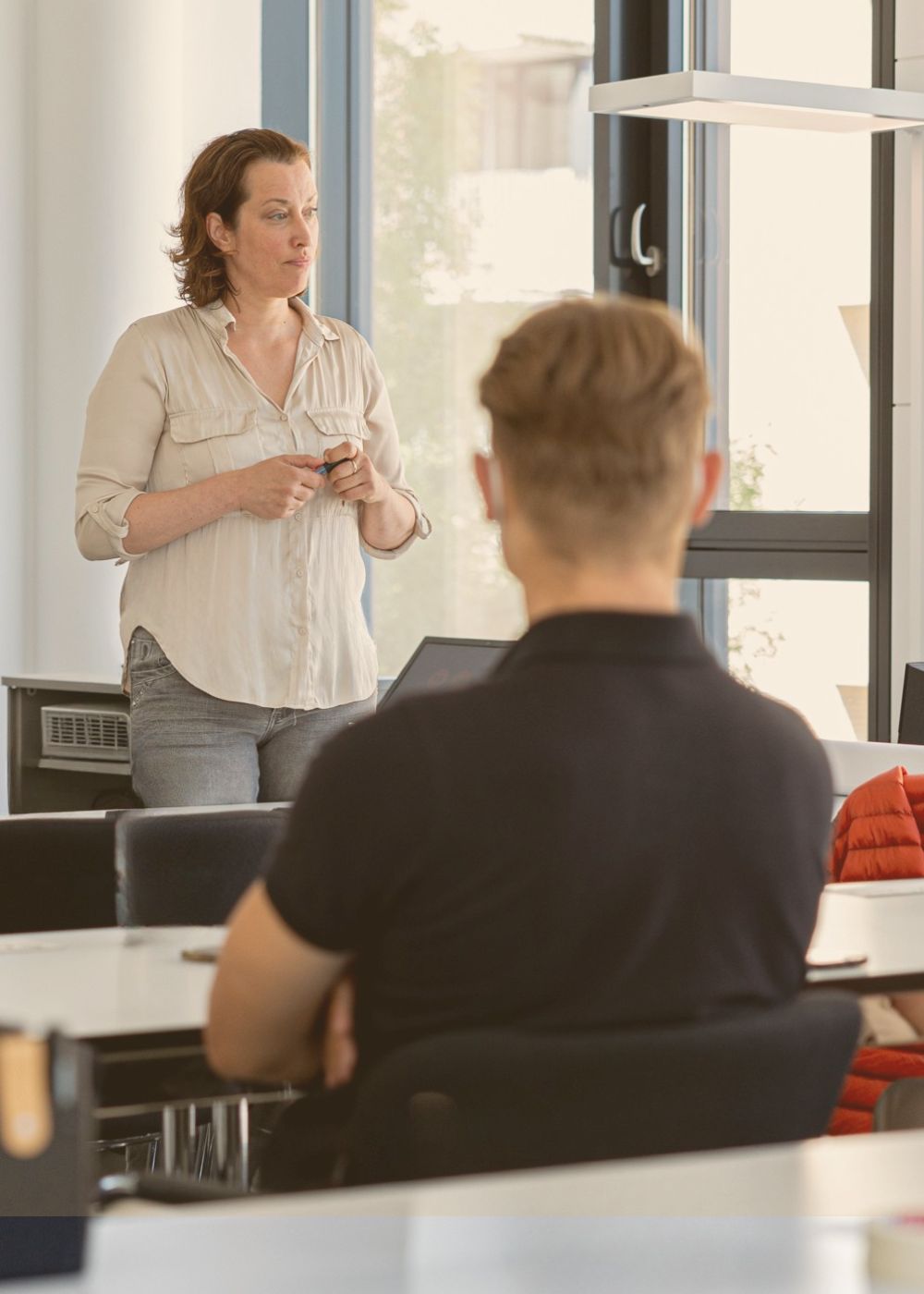 Julia Staffa steht in einem modernen Seminarraum vor einer Gruppe und spricht über agiles Arbeiten. 
