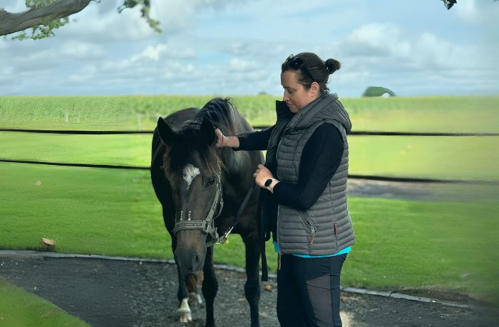 Julia steht mit einem schwarzen Pferd auf einem Reitplatz und streichelt es sanft am Kopf.