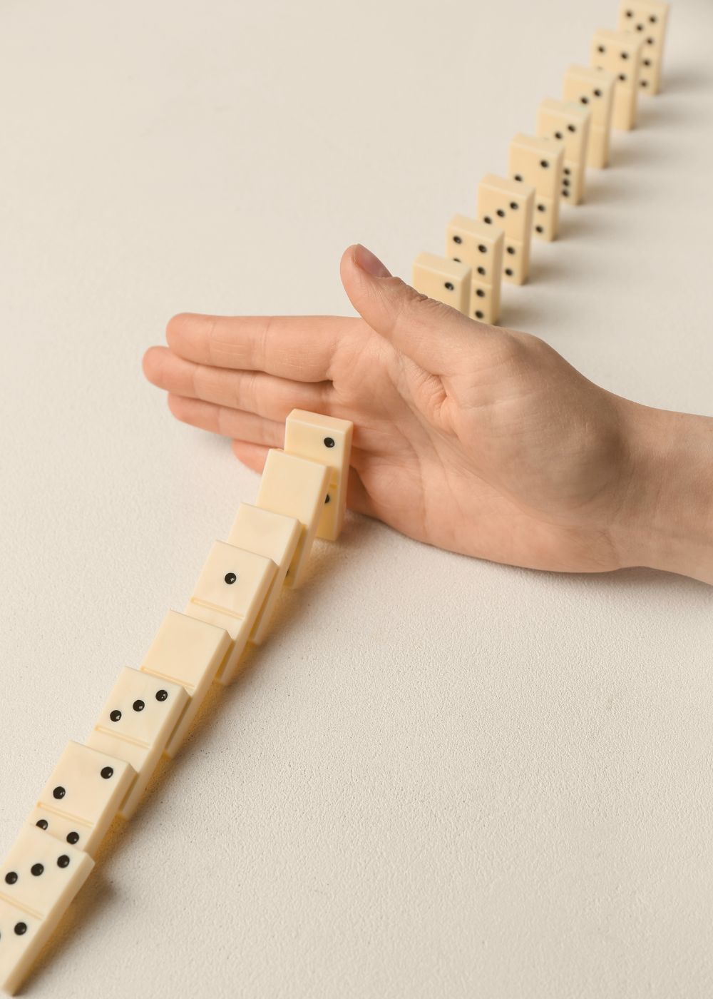 Eine Hand stoppt fallende Dominosteine – Symbol für das rechtzeitige Erkennen und Stoppen ineffizienter Abläufe. 