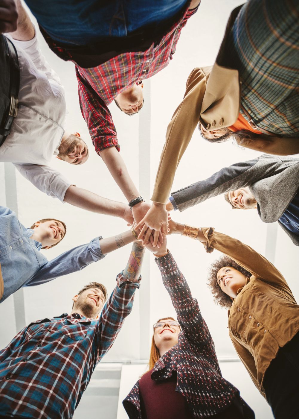 Ein Team steht im Kreis und streckt die Hände gemeinsam nach innen – Sinnbild für Zusammenhalt, Eigenverantwortung und kooperative Zusammenarbeit in selbstorganisierten Teams. 